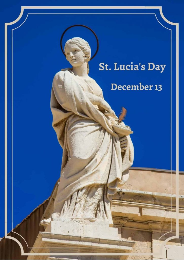 Statue of Santa Lucia in Italy.  She is standing and looking off to the left, facing the camera.  The sky is blue in the background.  You can part of a sand colored building in the background.