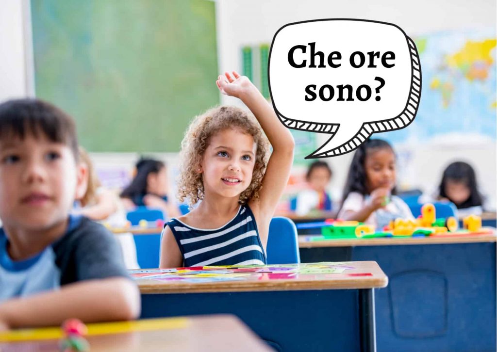 Girl in classroom raising her hand and asking with a graphic speech bubble, "Che ore sono?"  You can see other children at their desks in the background and a little boy at his desk in the foreground.  There are maps on the wall in the background.