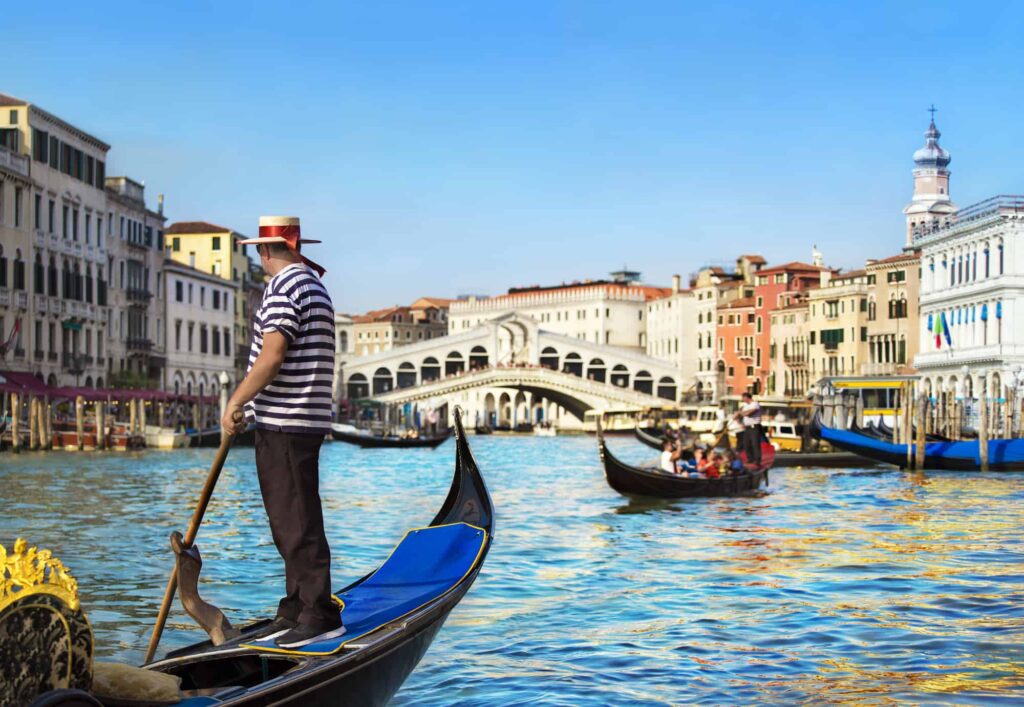 Gondolier on the Grand Canal in Venice, Italy.  He is wearing the traditional gondolier uniform that includes the paglietta, or straw hat.