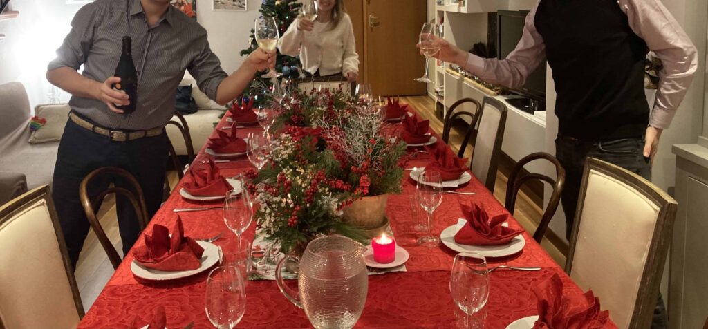 Table set for the cenone in Italy and guests are holding glasses for the New Year's Eve toast.