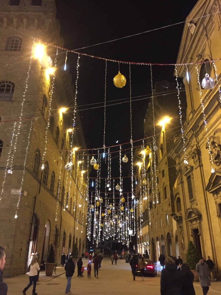 Twinkling lights are strung across the street in Florence, Italy and people are out walking.