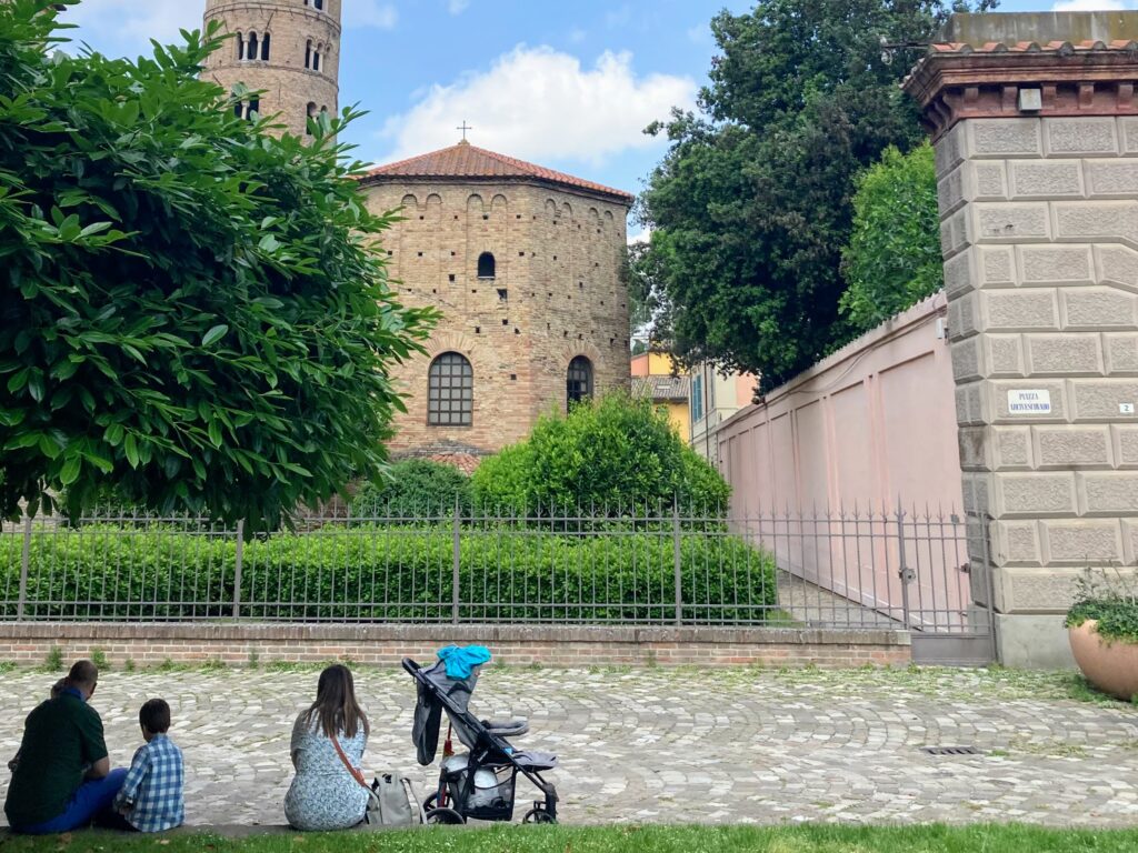 Family sitting outside in Ravenna, Italy. View of monument in front of them.