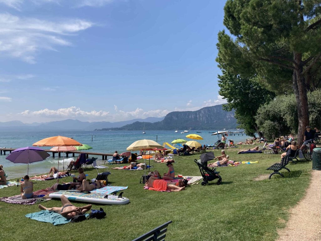 Grassy beach area with umbrellas and people enjoying the sun in Bardolino, Italy.