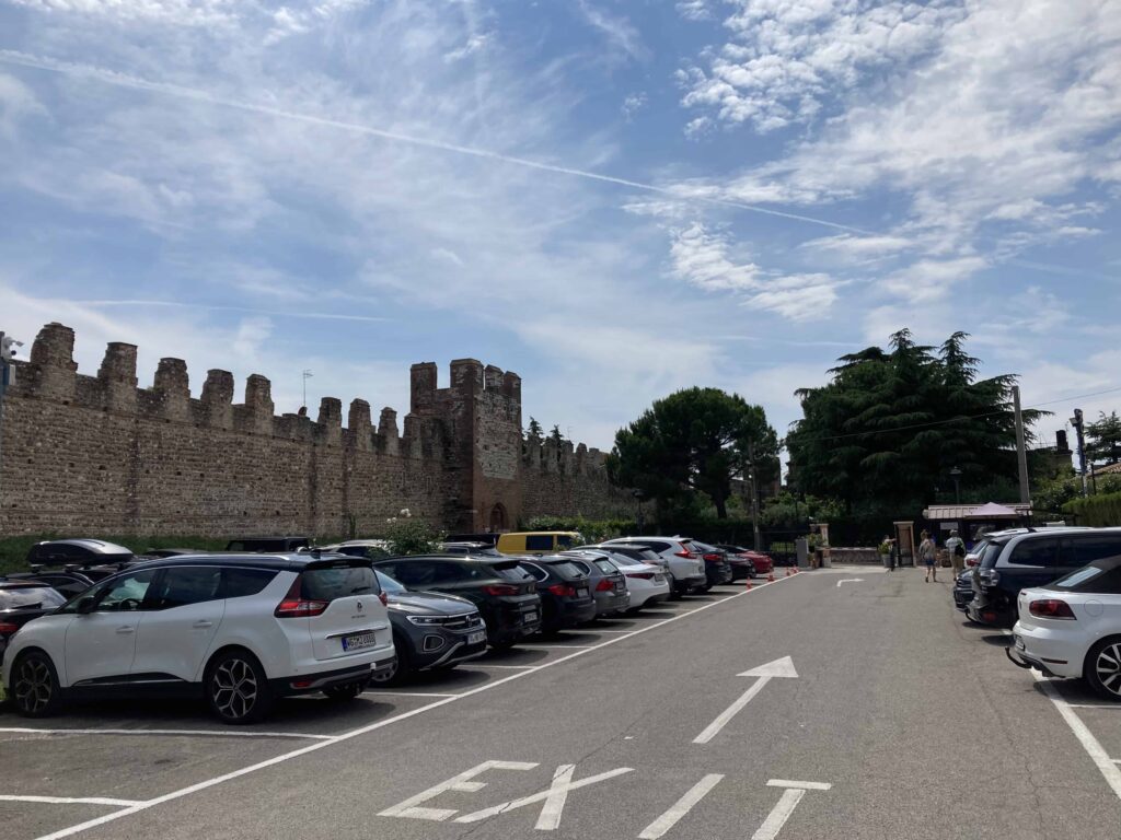 Parking lot with old city fortress walls on left. This is the town of Lazise in Northern Italy.