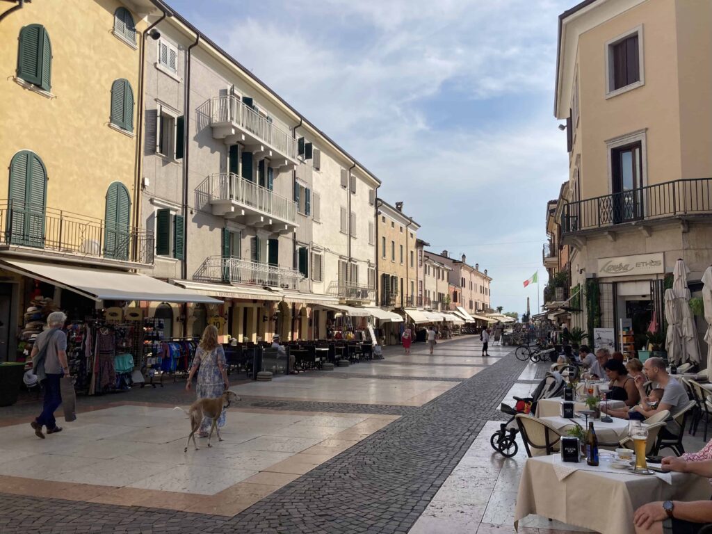 People sitting at cafes on either side of pedestrian street in Bardolino, Italy.