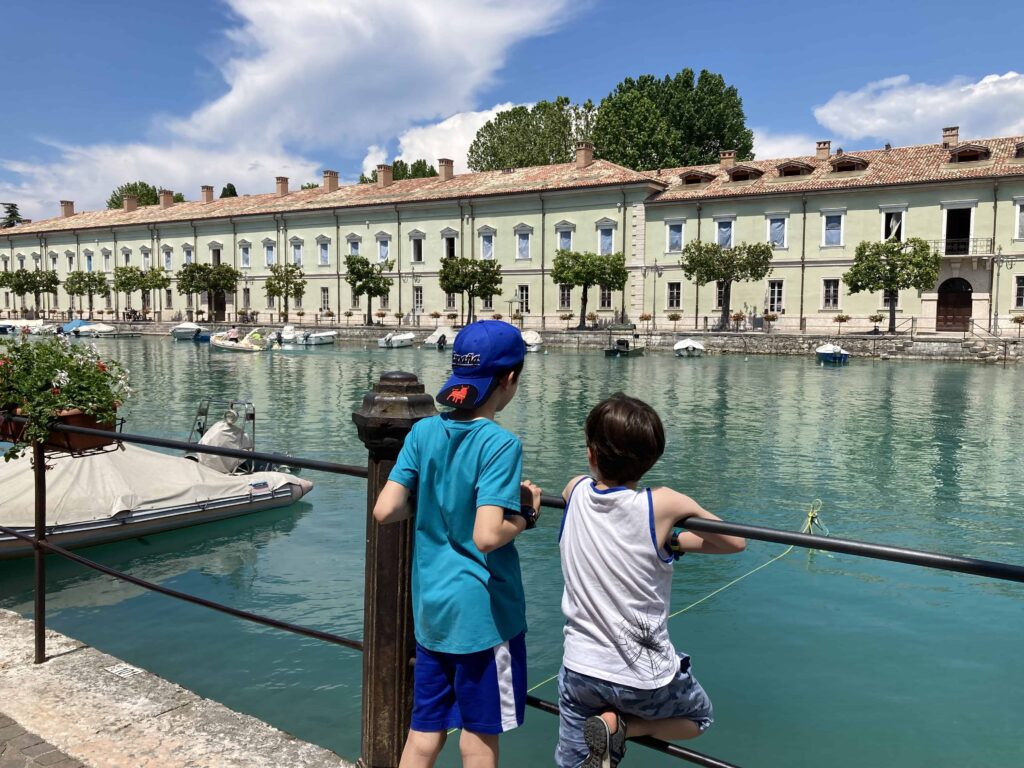Two boys at railing looking at canal of Lake Garda in Peschiera del Garda.