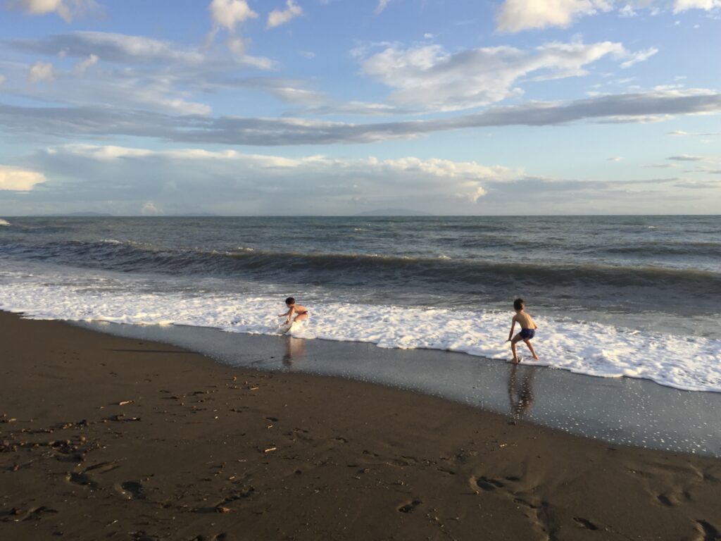 Two children playing at the beach in the edge of the water.