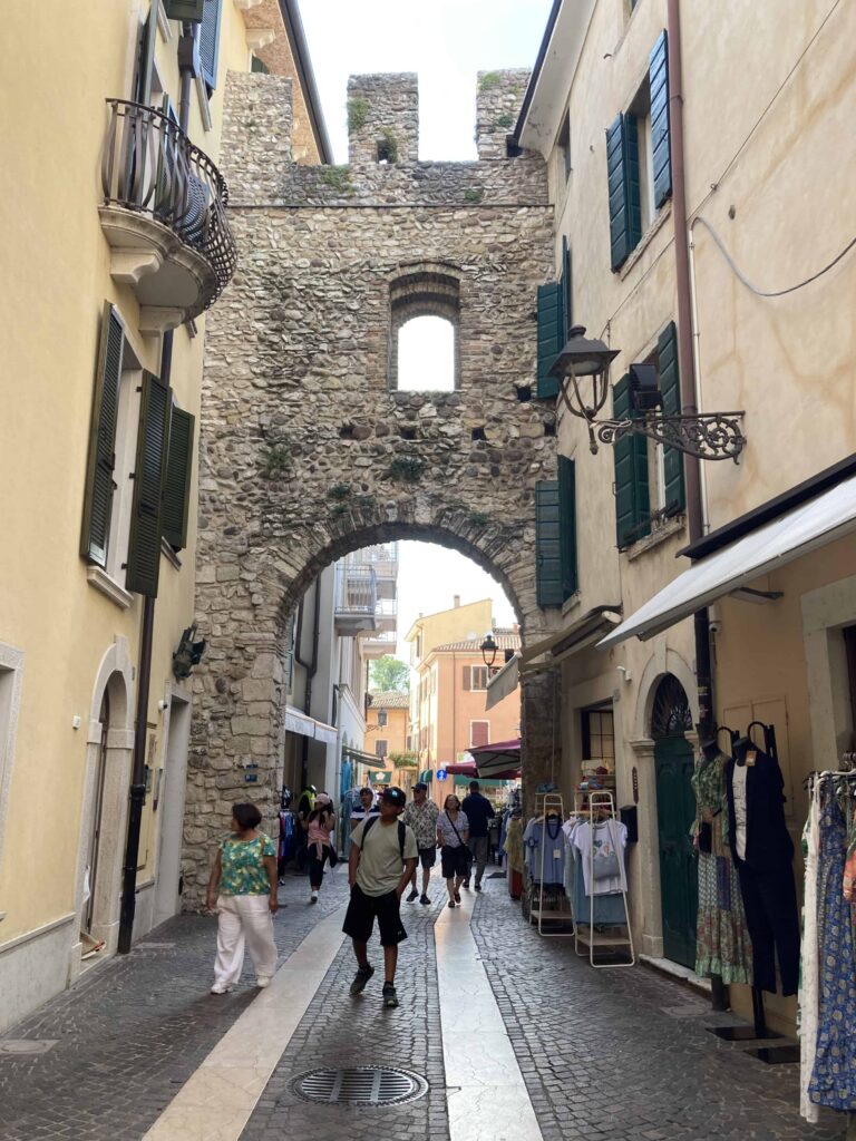 People walking through stone arch on narrow street in Bardolino in Lake Garda, Italy.
