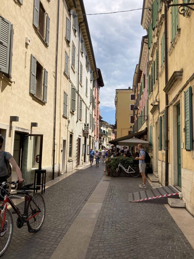 Narrow street with buildings on both sides in Peschiera del Garda. Cyclist in foreground walking bike.