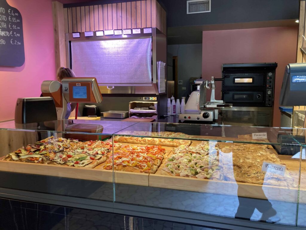 Pizza on display behind glass cases in a pizzeria in Lazise, Italy.