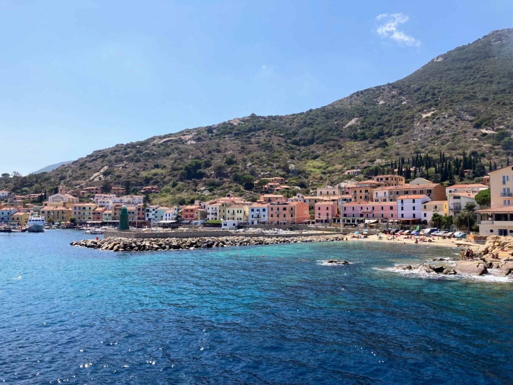 View of colorful seaside village on Giglio island. You can see sea, colorful homes, beach, and low mountains.