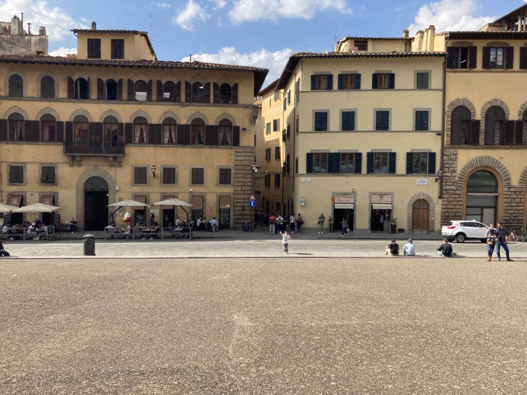 Empty Piazza Pitti looking toward buildings of Florence. There are a few people sitting and standing.