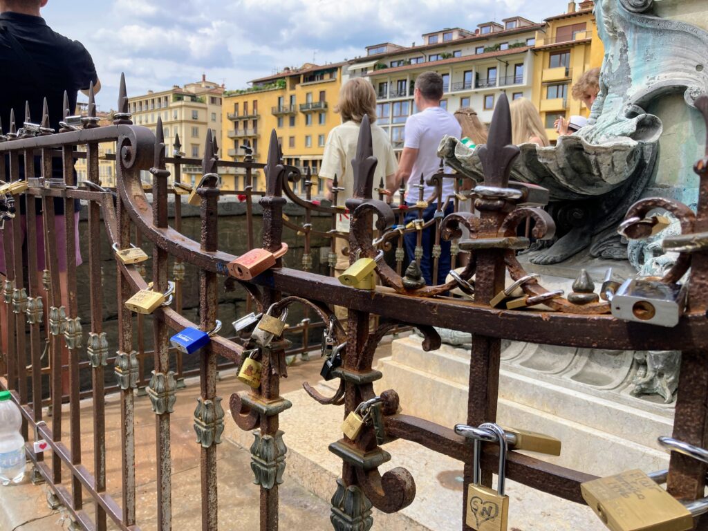 People walking on a bridge with padlocks on the iron railings.
