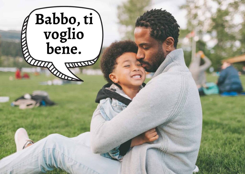 Father and son sitting on grass and hugging. Boy is saying 'babbo, ti voglio bene.'
