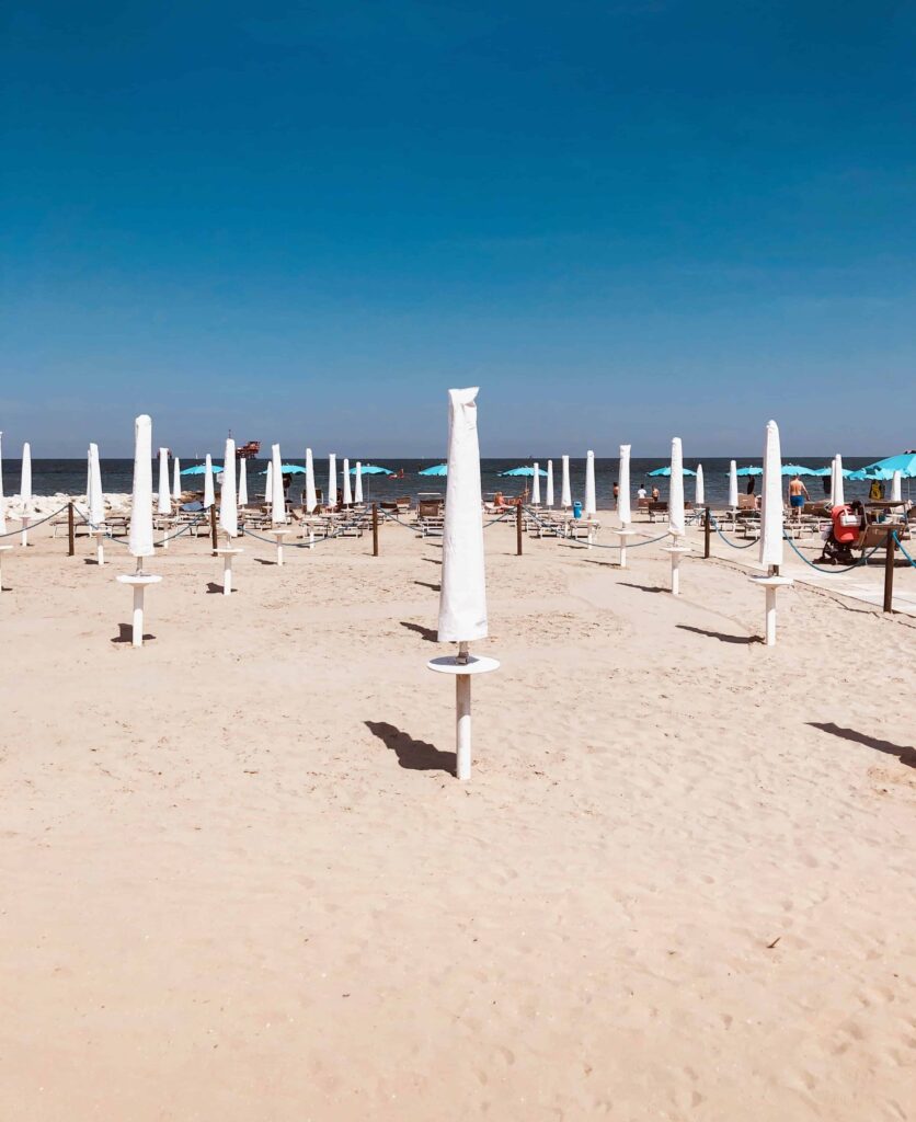 Beach club with closed umbrellas near Ravenna, Italy. There are a few people walking by the water.
