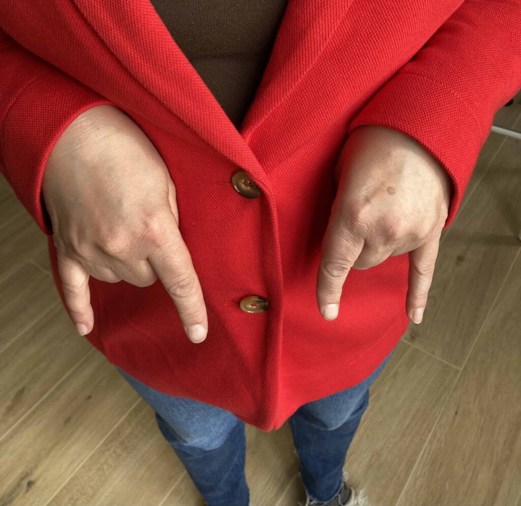 Close up of person in red coat and jeans giving the Italian hand gesture 'fare la corna'