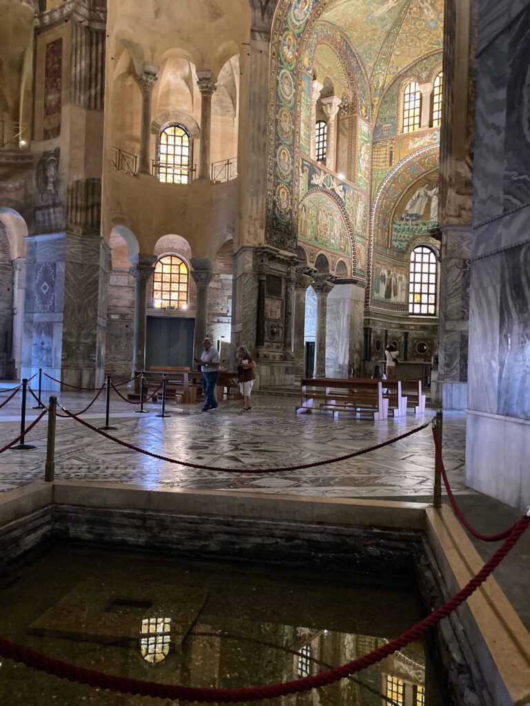 A couple walks inside the Basilica di San Vitale in Ravenna. You can see the colorful mosaics on the walls, ceiling, and floors.
