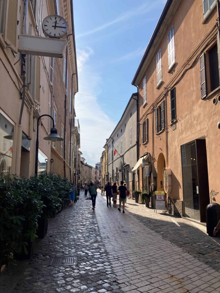 Pedestrians on cobblestone street in Ravenna, Italy. Buildings on either side. Sunny day.