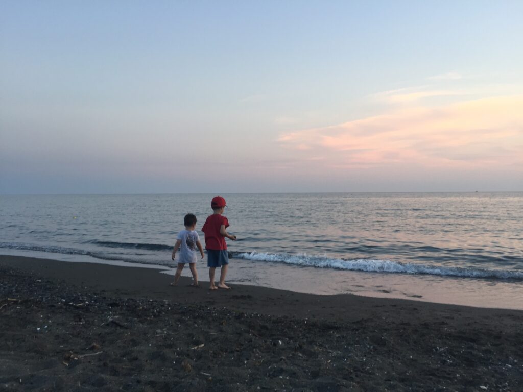 Two boys on the edge of the beach/sea in the evening.