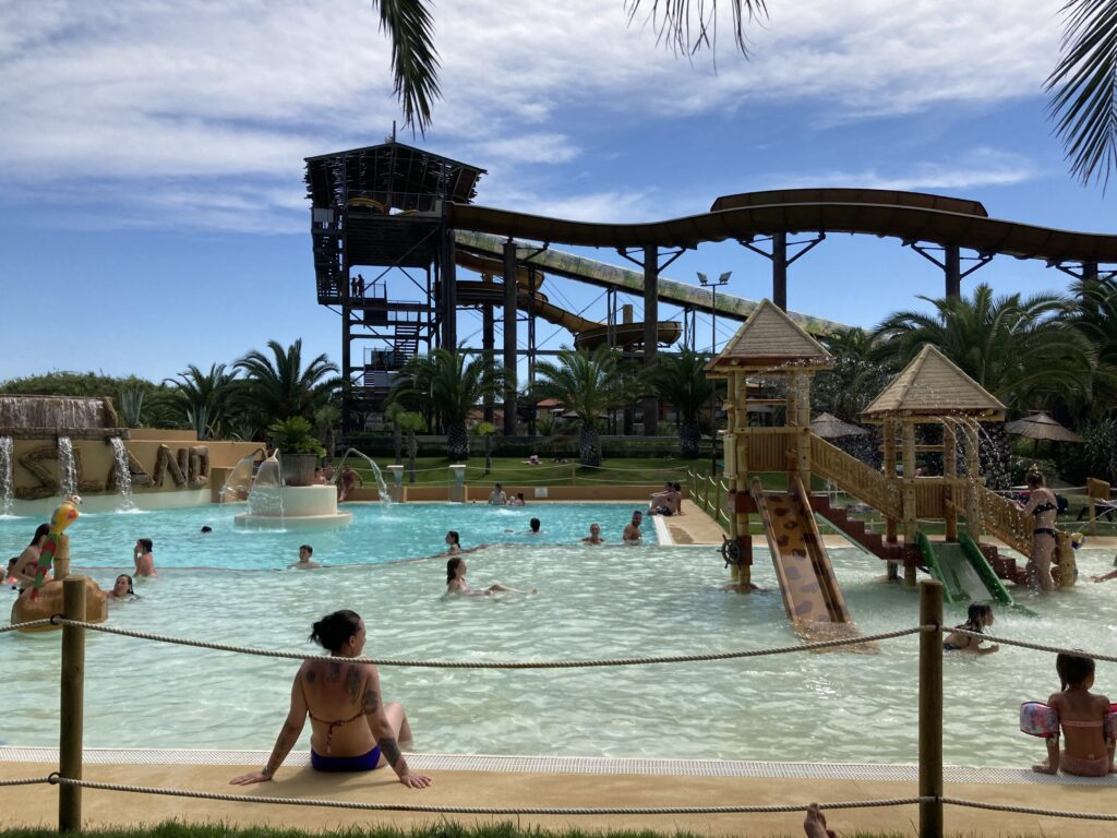 People at a water park. There's a large pool and a kids area. Large waterslides in the background.