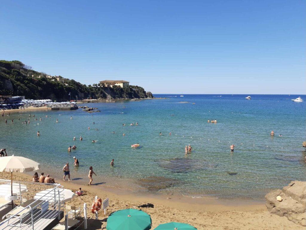 People swimming in turquoise water and sitting on a sandy beach on the Etruscan Coast in Italy.
