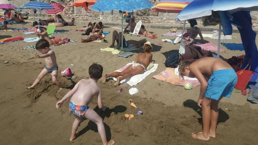 Kids playing in the sand at a beach in Tuscany. You can see beach umbrellas and people relaxing in the sun.