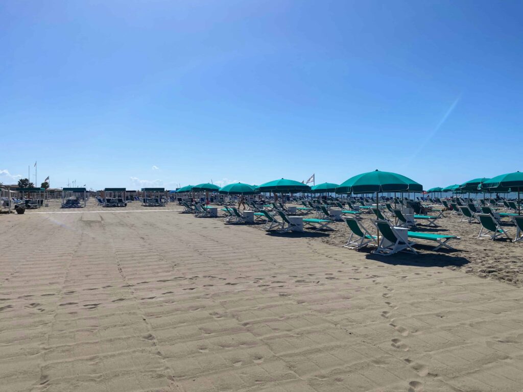 Green beach umbrellas and sun loungers line the raked sand at a beach club in Forte dei Marmi, Italy.