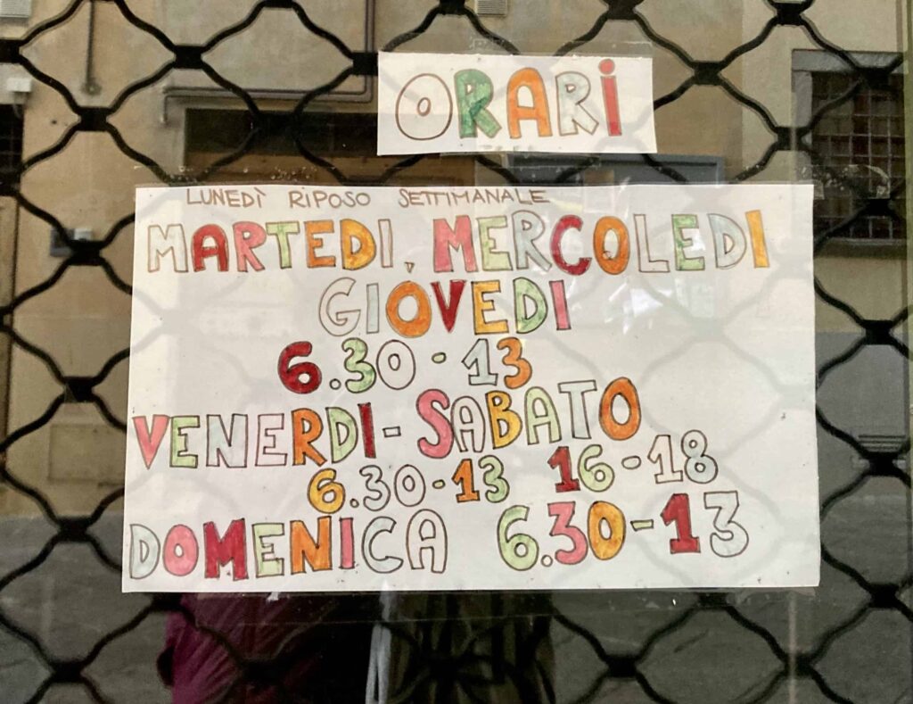 Colorful handwritten sign that shows opening days and hours for a store in Italy.
