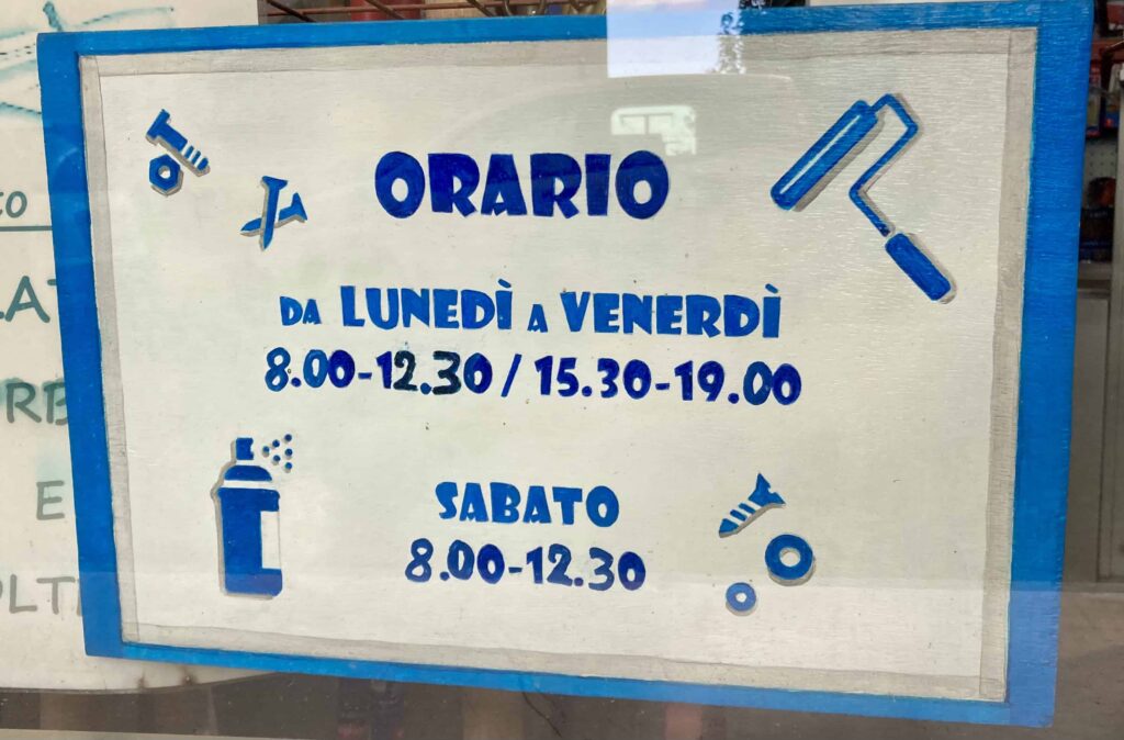 Sign in window of Italian hardware store listing opening days and hours.