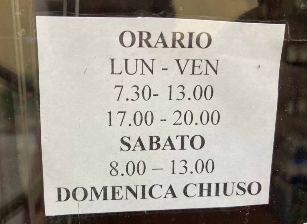 Sign in a window in Italy that lists the opening days and hours.