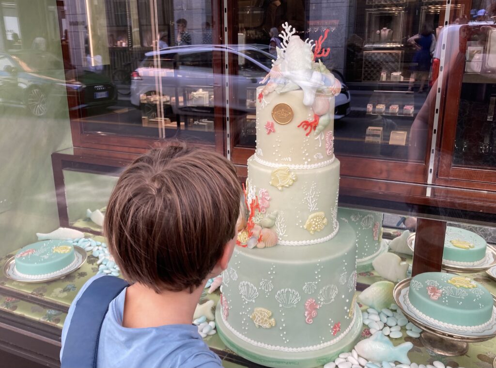 Boy looking at light green tiered cake in a pastry shop window in Milan, Italy.