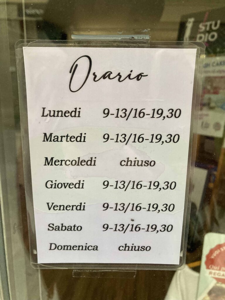 Sign in window in Italian store that lists opening days and hours.