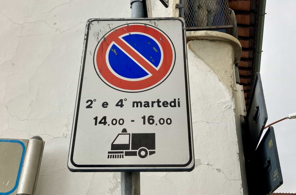 No parking and street cleaning sign in front of a wall in Italy.