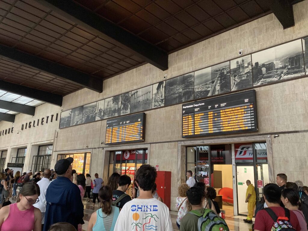 People wait in front of the digital departures and arrivals boards at the Florence train station.