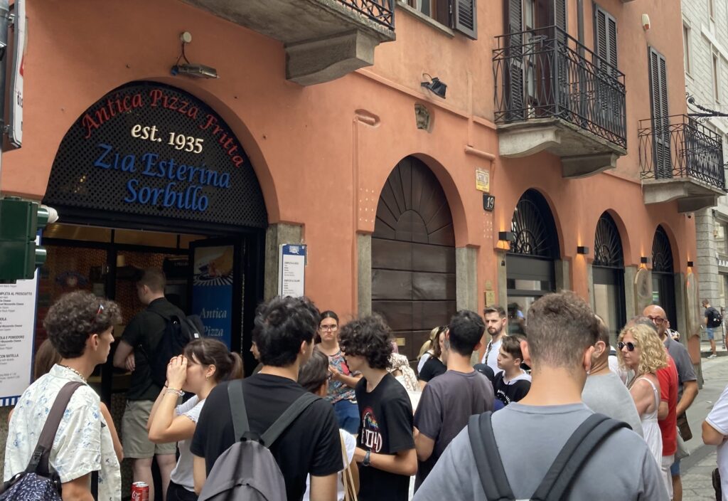 People waiting in line outside Pizza Fritta Sorbillo in MIlan, Italy. The building is orange.
